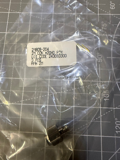 A small black metal electrical connector or terminal piece inside a clear plastic bag with a white product label, placed on a gray gridded cutting mat.
