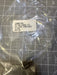 A small black metal electrical connector or terminal piece inside a clear plastic bag with a white product label, placed on a gray gridded cutting mat.
