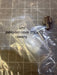 A small metal connector fitting in a clear plastic bag with printed part number text, placed on a gridded surface.