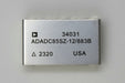 A rectangular silver metal electronic component with black printed text including '34031', 'AD2700UD', '/883B', '2320', and 'USA', photographed on a beige surface.