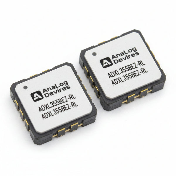 Two ADXL355BEZ-RL small electronic integrated circuit chips on a white background, one showing a white label with black text and the other showing the gold and gray solder pads of the chip.