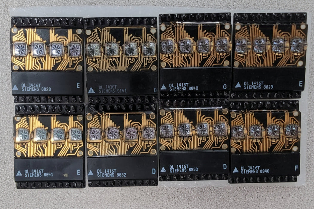Six black electronic circuit boards with gold traces and silver crystal components, arranged in two rows of three on a light gray textured surface.