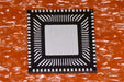 FT2232HQ electronic microchip with a black outer border, white pin points, and a silver center, placed on a textured orange surface.