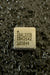 A square integrated circuit chip with black printed text reading 'ADXL355B #2542 105844' on a beige surface, set against a dark textured background.