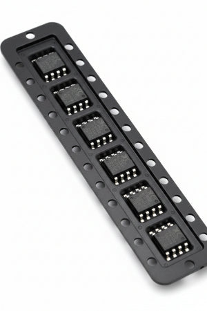A strip of black electronic integrated circuit chips with silver pins, positioned vertically against a pink textured background.